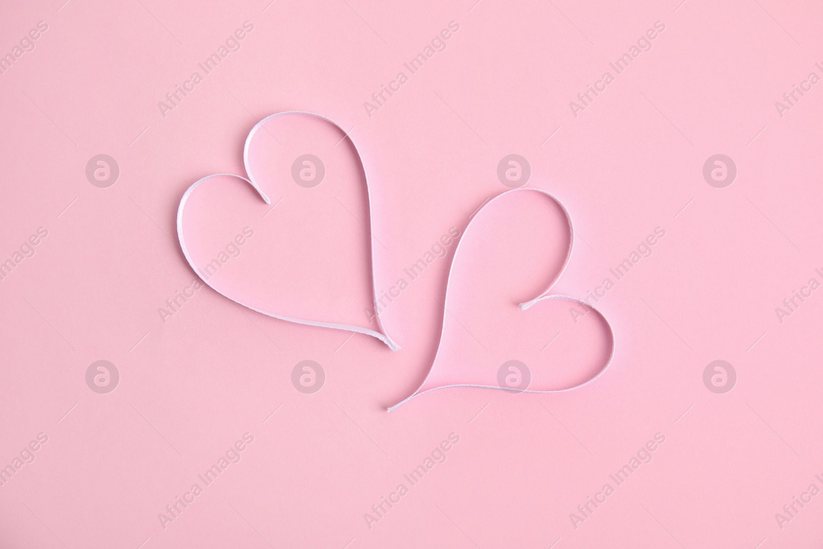 Photo of Hearts made of white ribbon on pink background, flat lay. Valentine's day celebration
