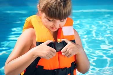 Photo of Little girl putting on orange life vest in swimming pool