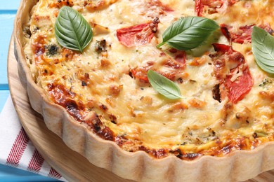 Photo of Tasty quiche with tomatoes, basil and cheese on light blue table, closeup