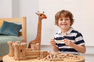 Photo of Cute little boy playing with wooden construction set at table in room. Child's toy