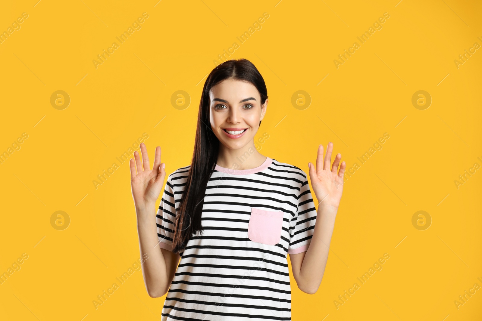 Photo of Attractive young woman showing hello gesture on yellow background