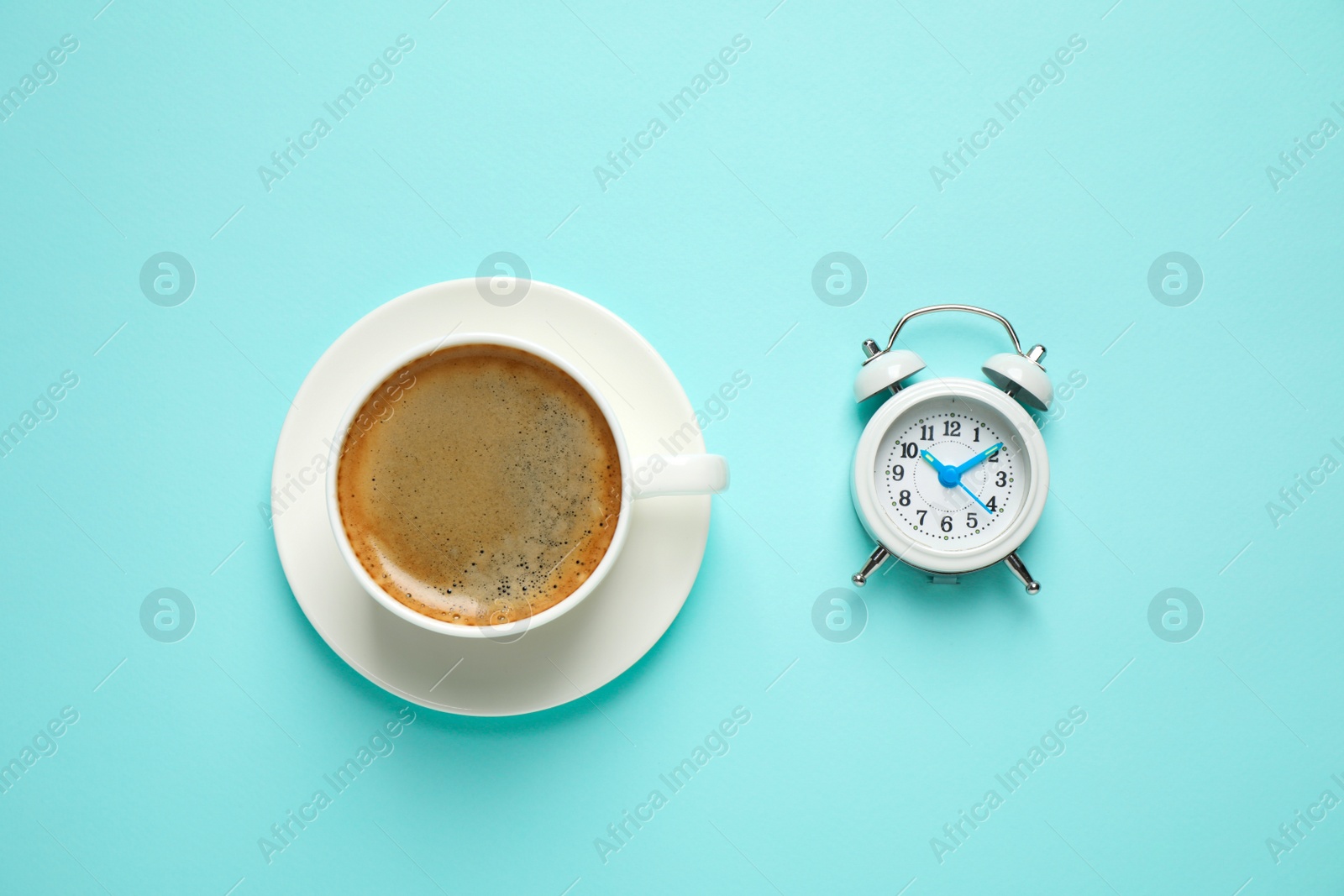 Photo of Cup of morning coffee and alarm clock on light blue background, flat lay