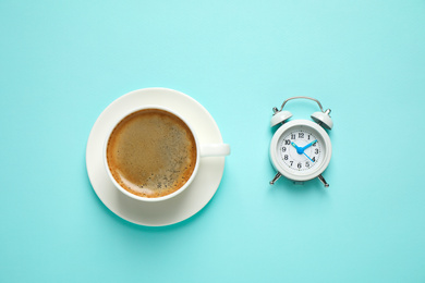 Cup of morning coffee and alarm clock on light blue background, flat lay