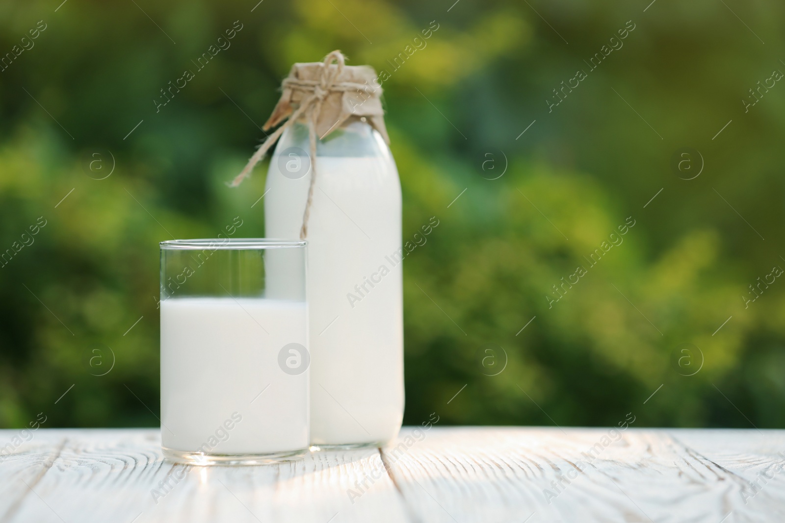 Photo of Bottle and glass of tasty fresh milk on white wooden table against blurred background, space for text