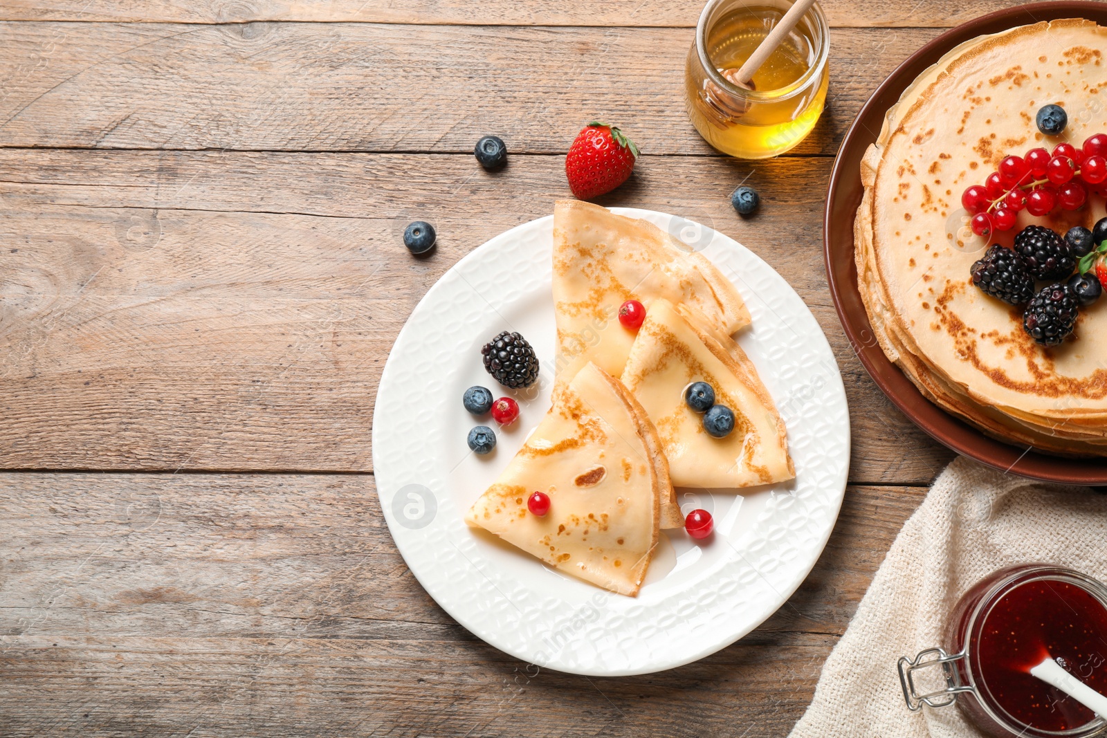 Photo of Delicious thin pancakes with berries on wooden table, flat lay. Space for text