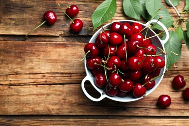 Photo of Wet red cherries in colander on wooden table, flat lay. Space for text