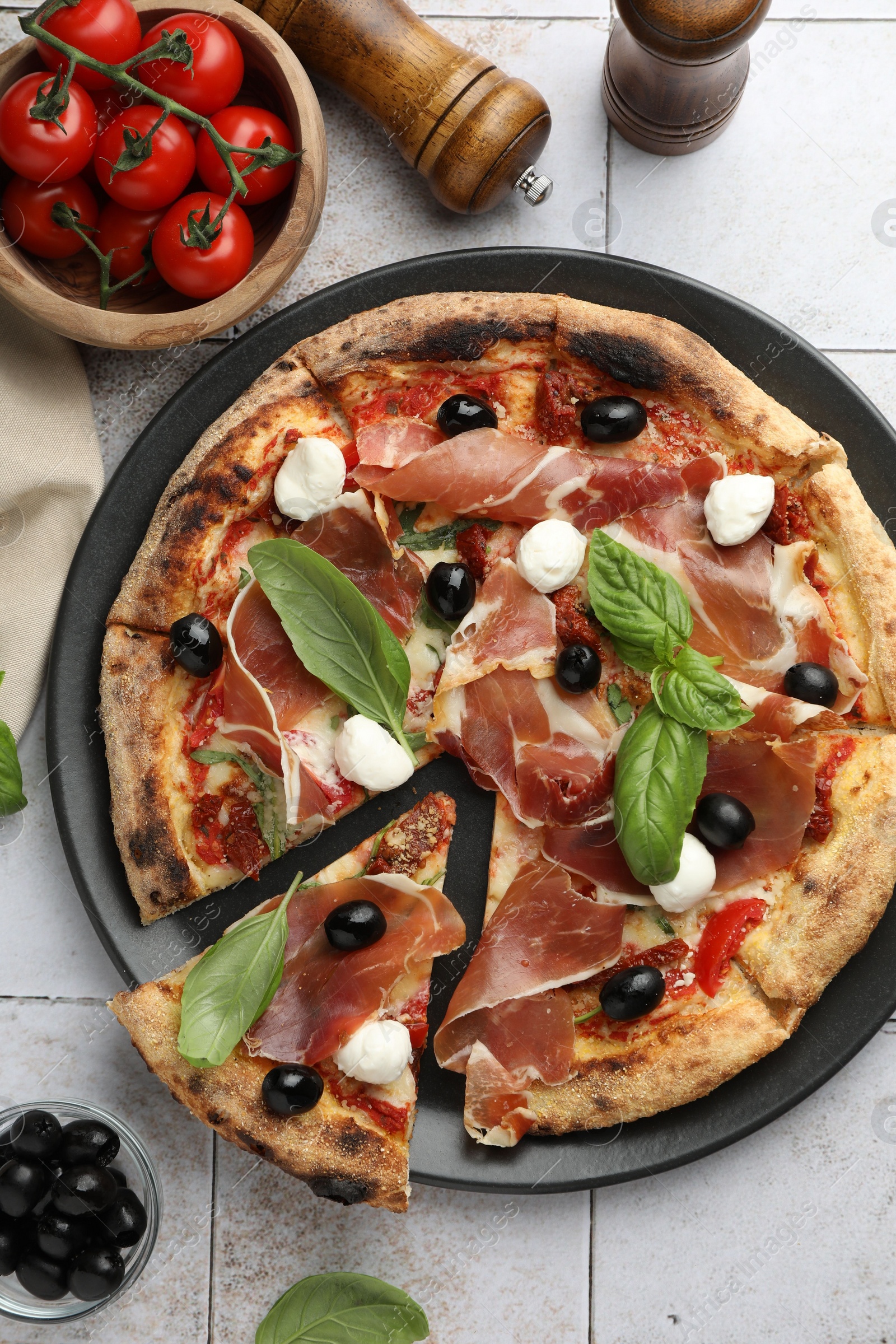 Photo of Tasty pizza with cured ham, olives, mozzarella cheese, tomatoes and basil on light tiled table, flat lay