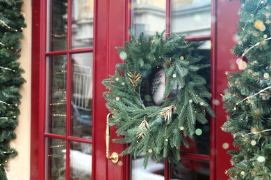 Photo of Beautiful Christmas wreath hanging on red glass door