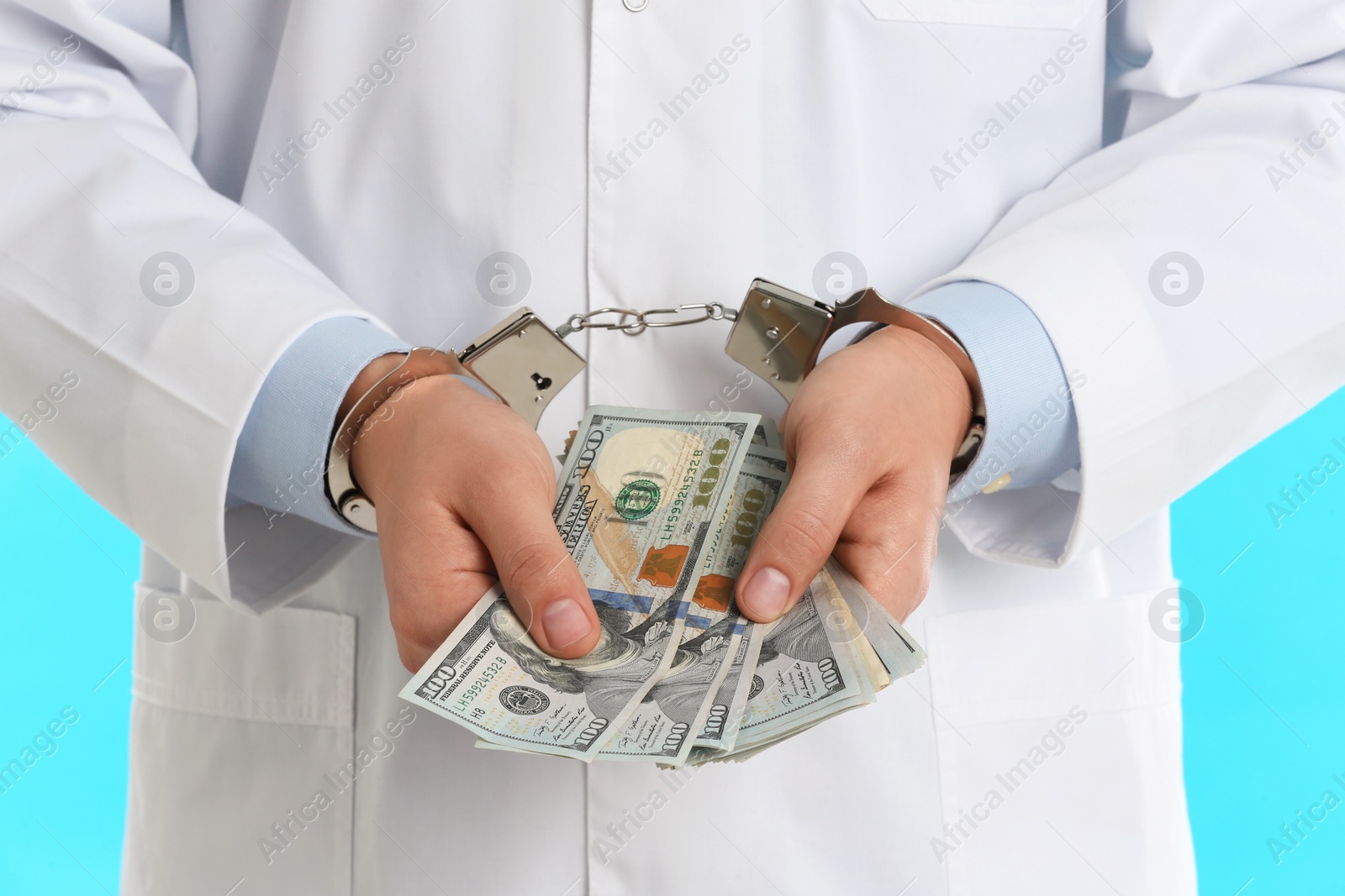 Photo of Doctor in handcuffs with bribe on light blue background, closeup. Corrupted medicine