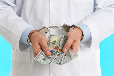 Doctor in handcuffs with bribe on light blue background, closeup. Corrupted medicine