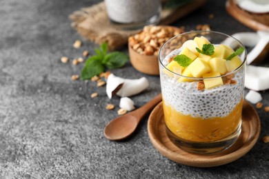 Photo of Delicious chia pudding with mango, mint and granola on grey table, space for text