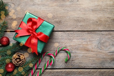 Photo of Gift box, candy canes, fir tree branches and Christmas decor on wooden table, flat lay. Space for text