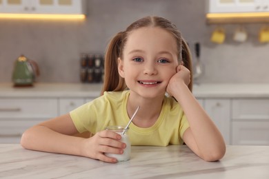 Photo of Cute little girl with tasty yogurt at white marble table in kitchen