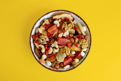 Bowl with mixed dried fruits and nuts on yellow background, top view