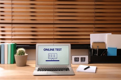 Photo of Laptop with online test on wooden desk in office