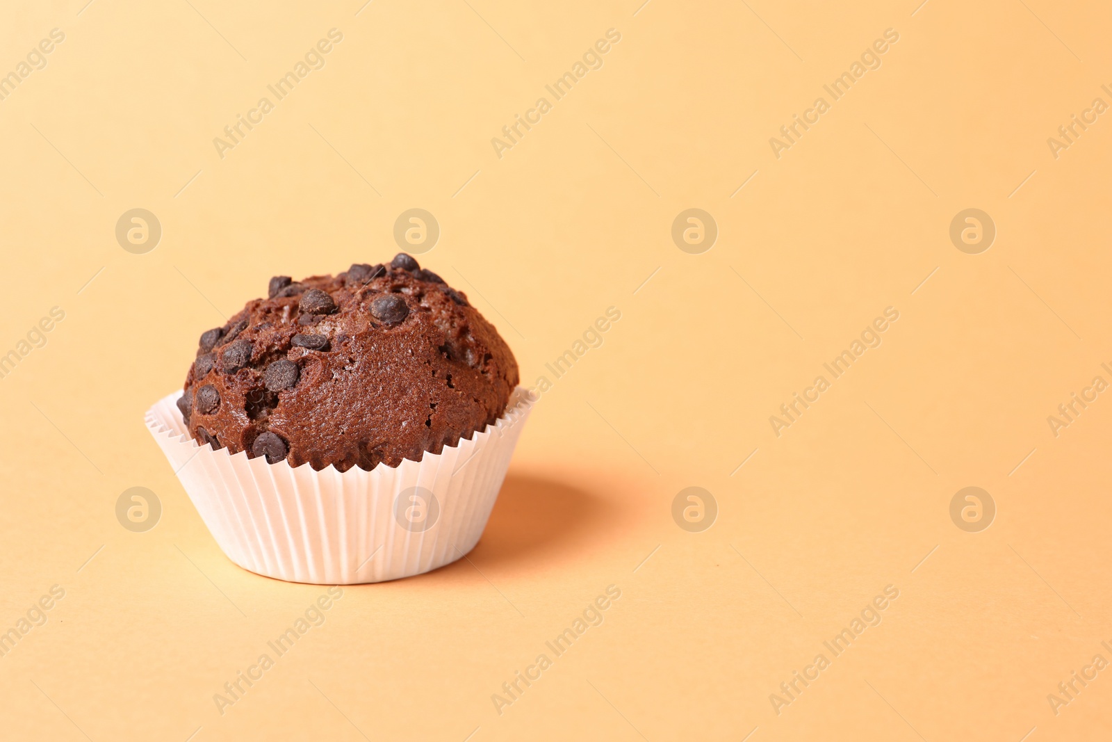 Photo of Tasty chocolate muffin on pale orange background, space for text