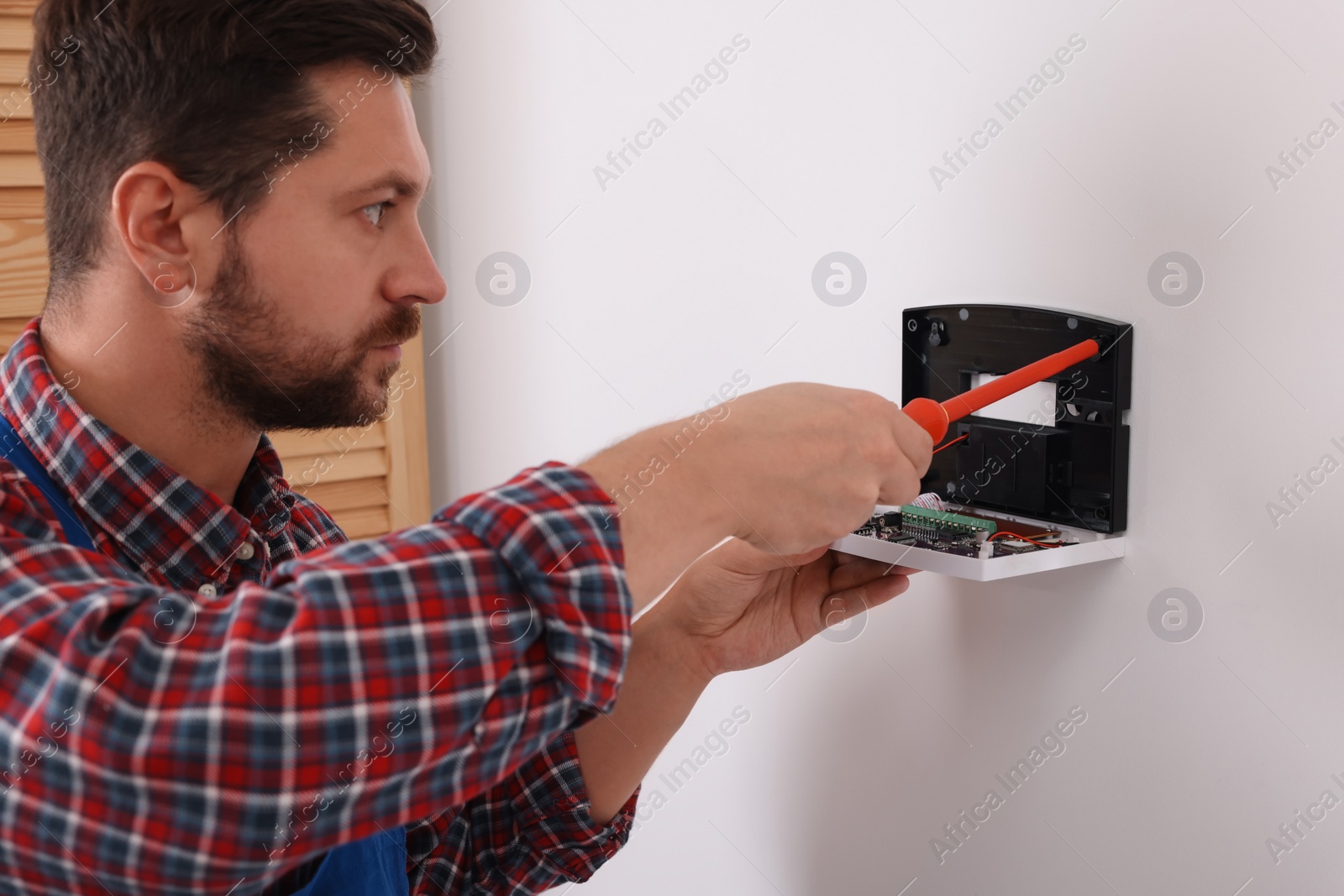 Photo of Technician installing home security alarm system on white wall indoors