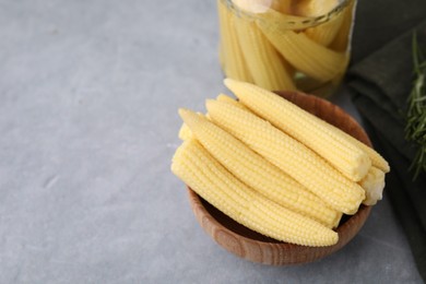 Tasty fresh yellow baby corns in bowl on grey table, space for text