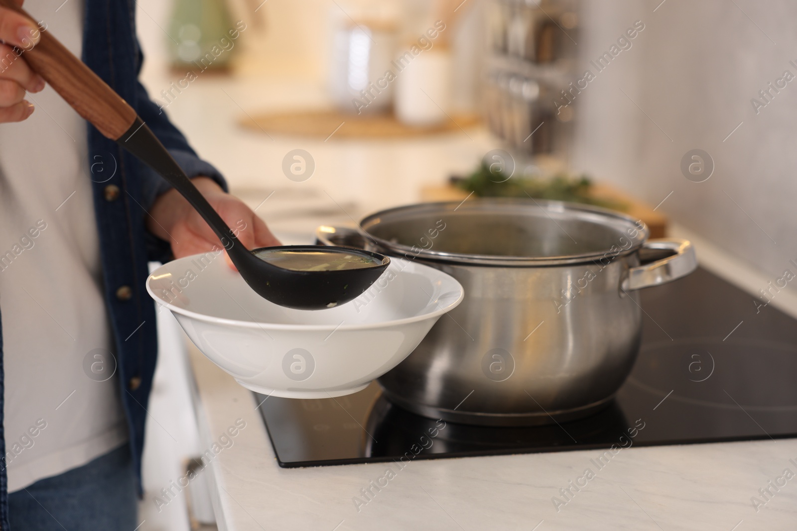 Photo of Woman pouring tasty soup into bowl at countertop in kitchen, closeup