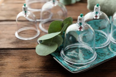 Cupping therapy. Plastic cups and eucalyptus leaves on wooden table, closeup. Space for text