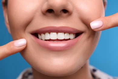 Photo of Young woman with beautiful smile on blue background, closeup. Cosmetic dentistry
