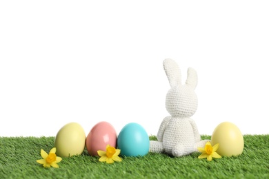 Photo of Cute Easter bunny toy and dyed eggs on green grass against white background, space for text