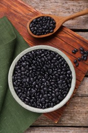 Bowl and spoon of raw black beans on wooden table, flat lay