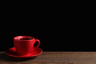 Red cup with aromatic coffee on wooden table against black background. Space for text