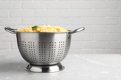 Cooked pasta in metal colander on grey marble table. Space for text