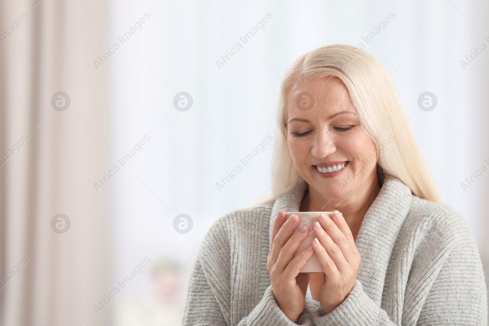 Photo of Portrait of beautiful older woman with cup of tea against blurred background. Space for text