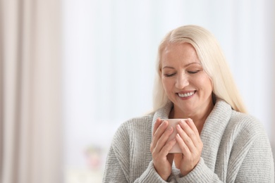 Photo of Portrait of beautiful older woman with cup of tea against blurred background. Space for text