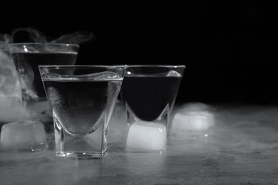 Vodka in shot glasses with ice on table against black background, closeup. Space for text