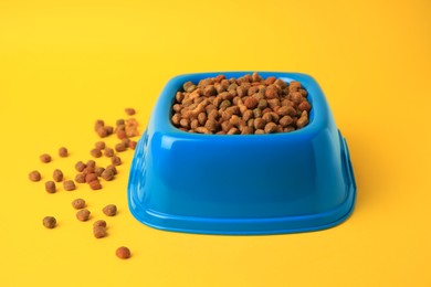 Photo of Dry pet food in feeding bowl on yellow background