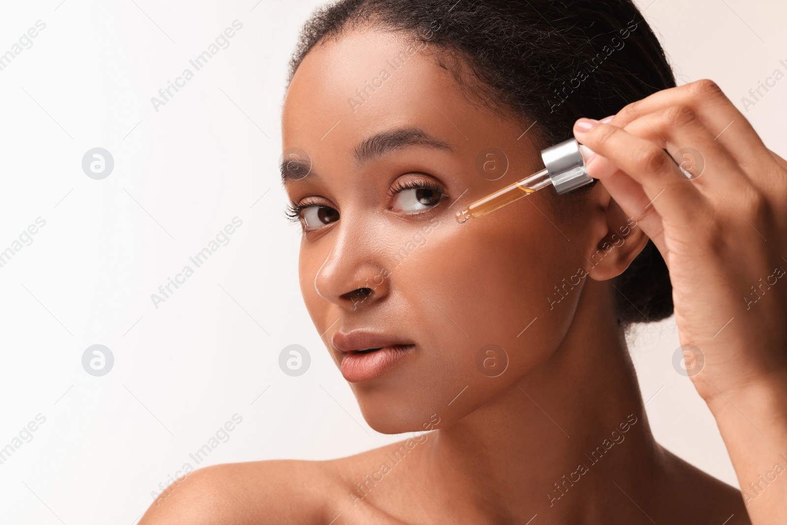 Photo of Beautiful woman applying serum onto her face on white background, closeup. Space for text