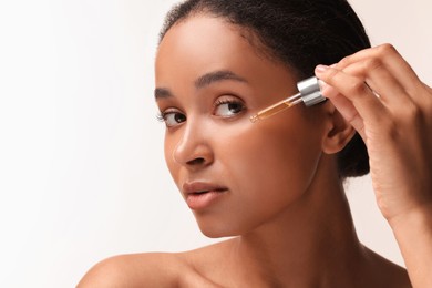 Photo of Beautiful woman applying serum onto her face on white background, closeup. Space for text