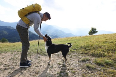 Photo of Tourist with backpack and trekking poles petting cute dog in mountains