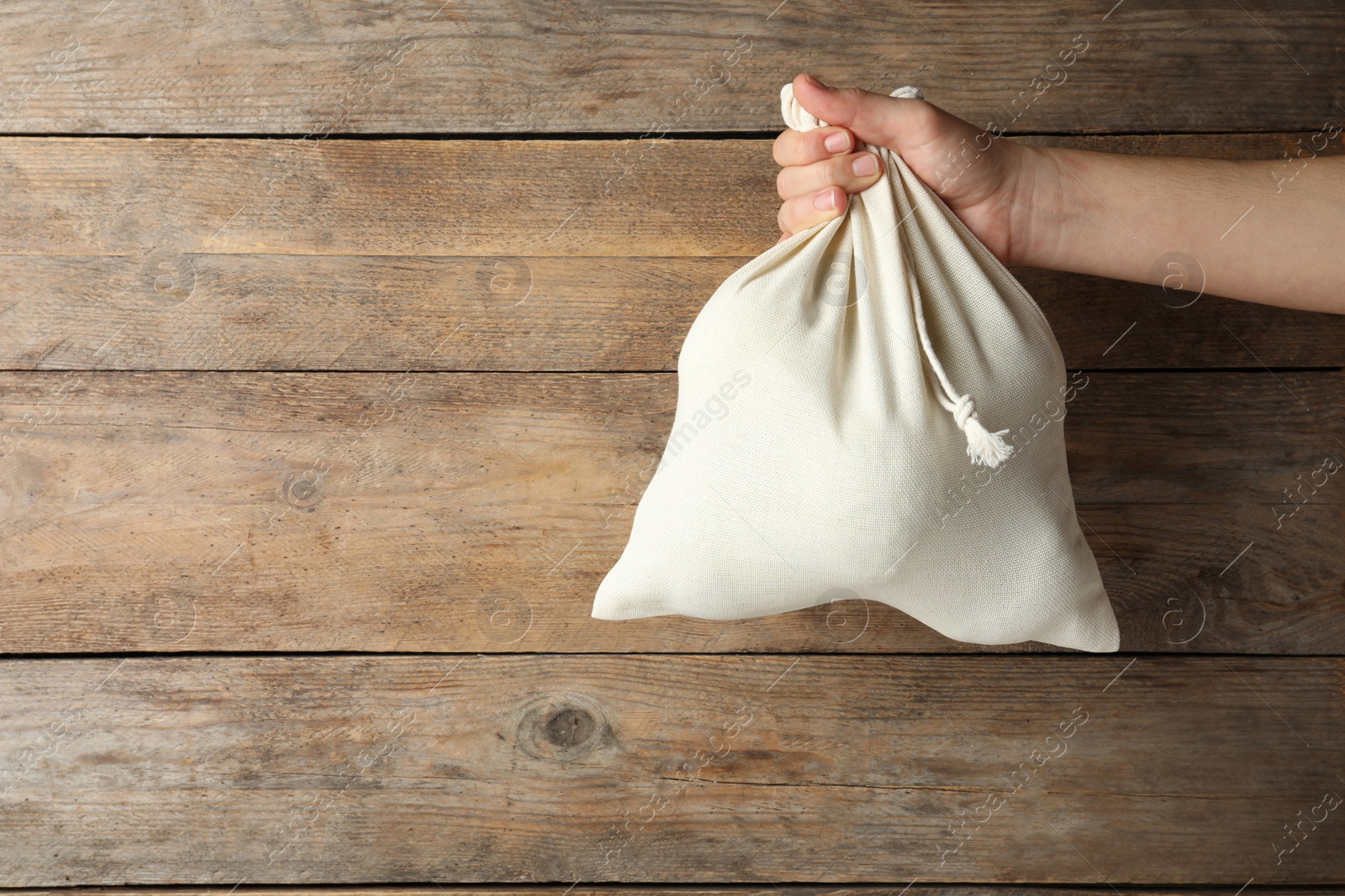 Photo of Woman holding full cotton eco bag on wooden background, closeup. Space for text