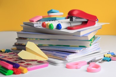 Photo of Many books, paper plane and different school stationery on white table against orange background. Back to school