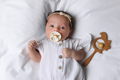 Cute little baby with pacifier and rattle lying on bed, top view