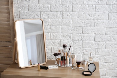 Makeup cosmetic products and tools on dressing table near brick wall with space for text