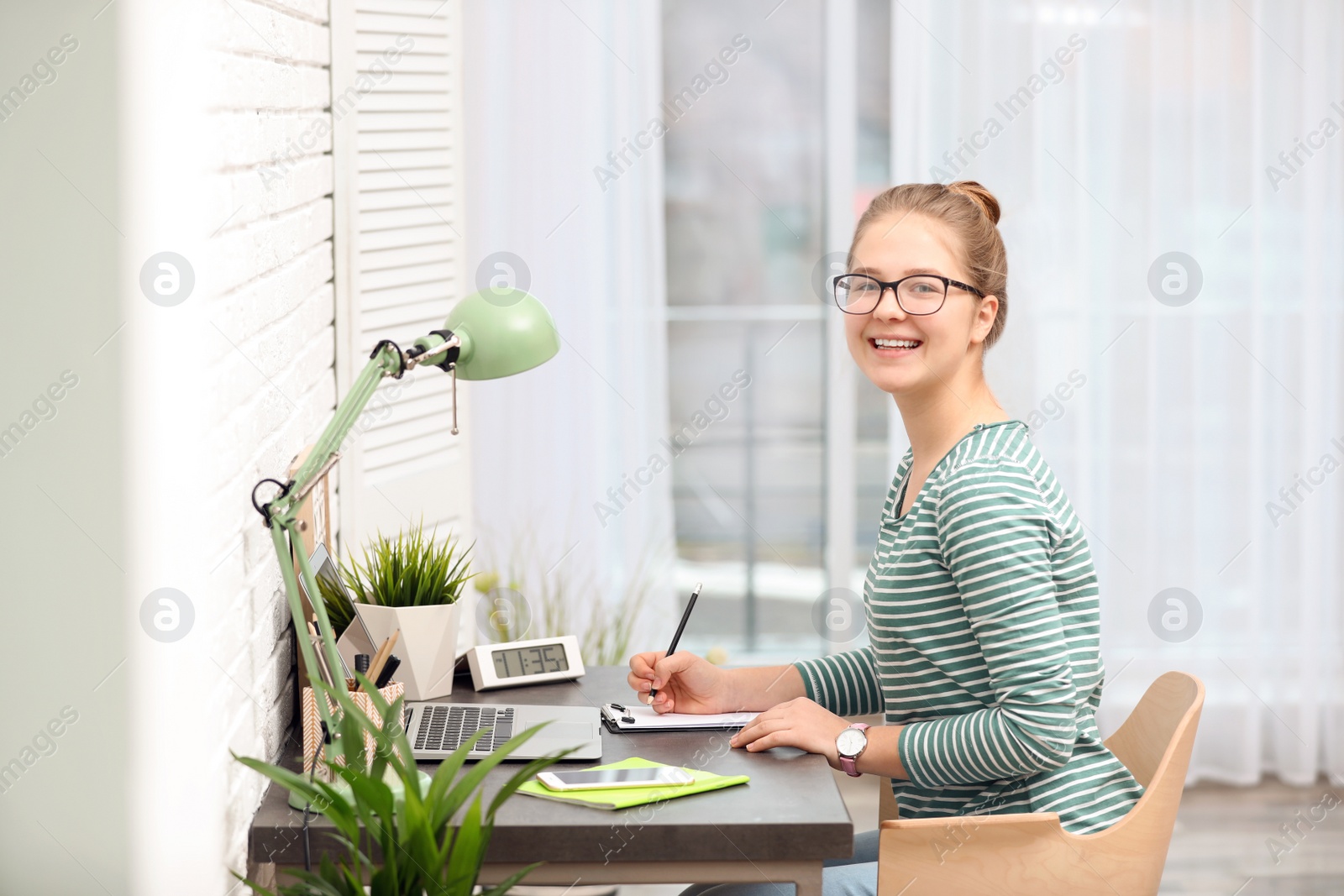 Photo of Pretty teenage girl doing homework at table in room