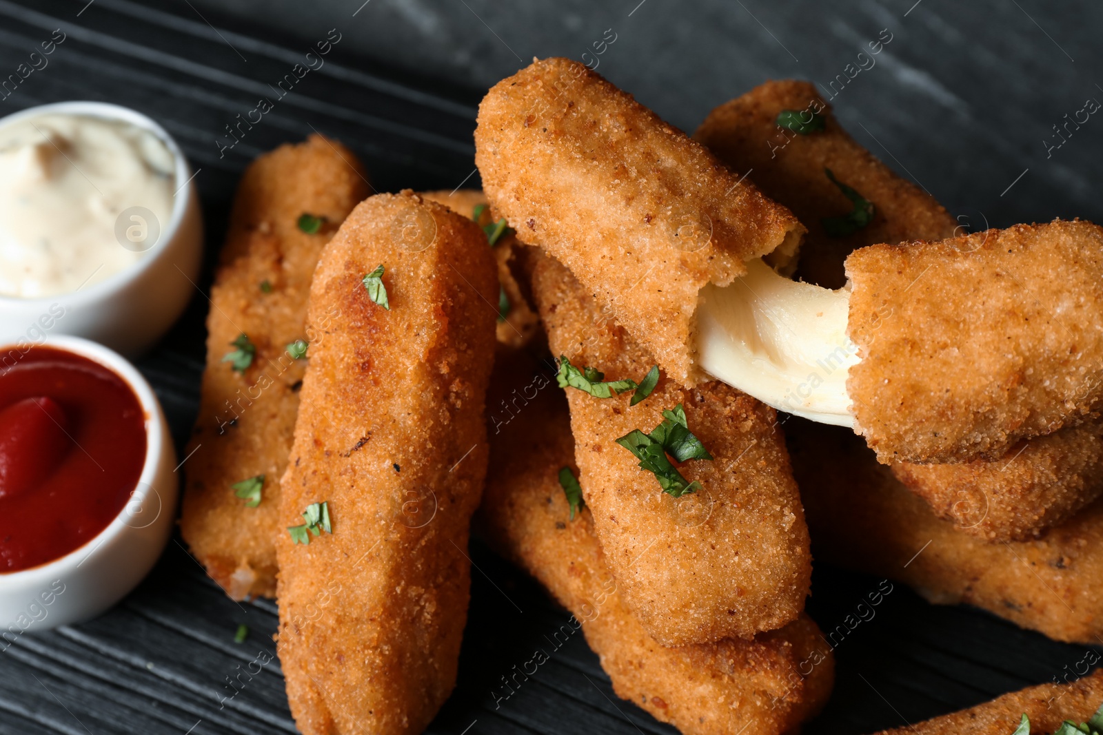 Photo of Pile of tasty cheese sticks and sauces on table, closeup