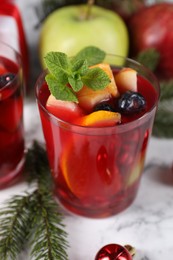 Photo of Aromatic Sangria drink in glass, ingredients and Christmas decor on white marble table