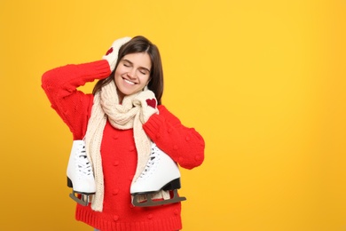 Photo of Happy woman with ice skates on yellow background. Space for text