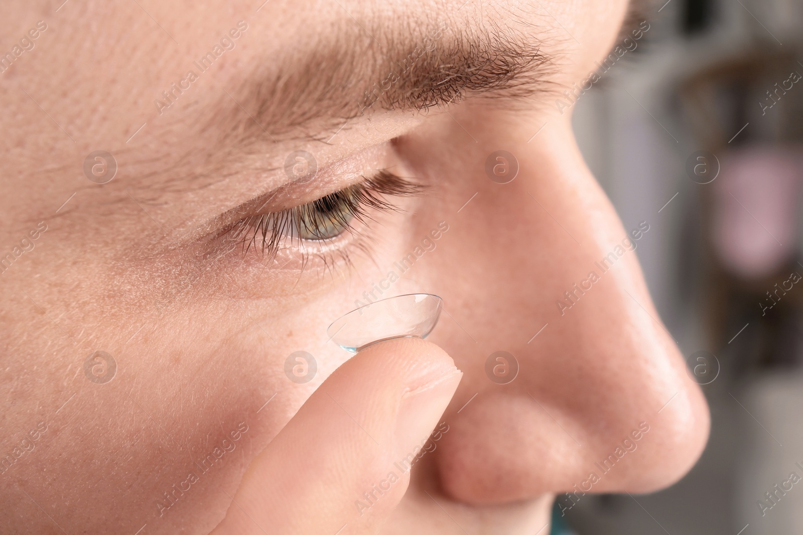 Photo of Young man putting contact lens into his eye, closeup