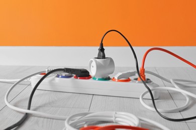 Power strip with different electrical plugs on white laminated floor near orange wall