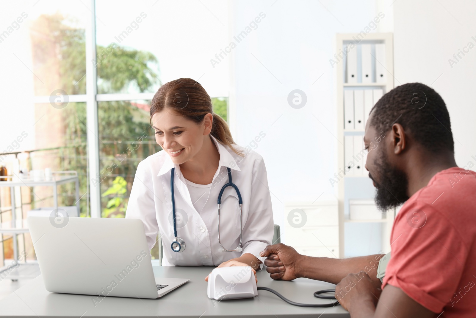 Photo of Young doctor checking African-American patient's blood pressure in hospital