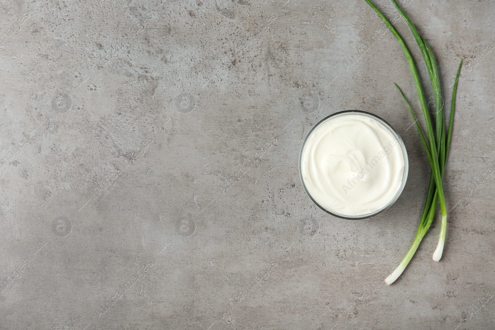 Photo of Glass bowl of fresh sour cream with green onion on grey table, flat lay. Space for text