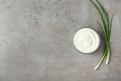 Glass bowl of fresh sour cream with green onion on grey table, flat lay. Space for text