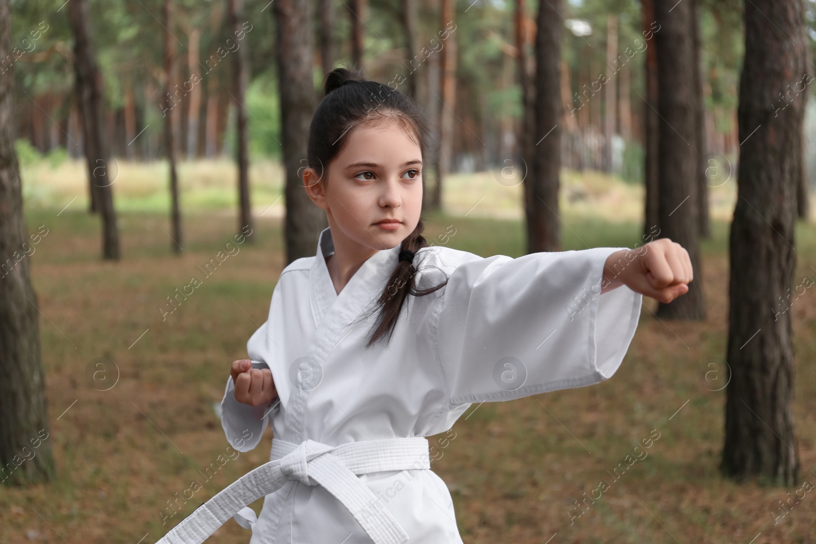 Photo of Cute little girl in kimono practicing karate in forest